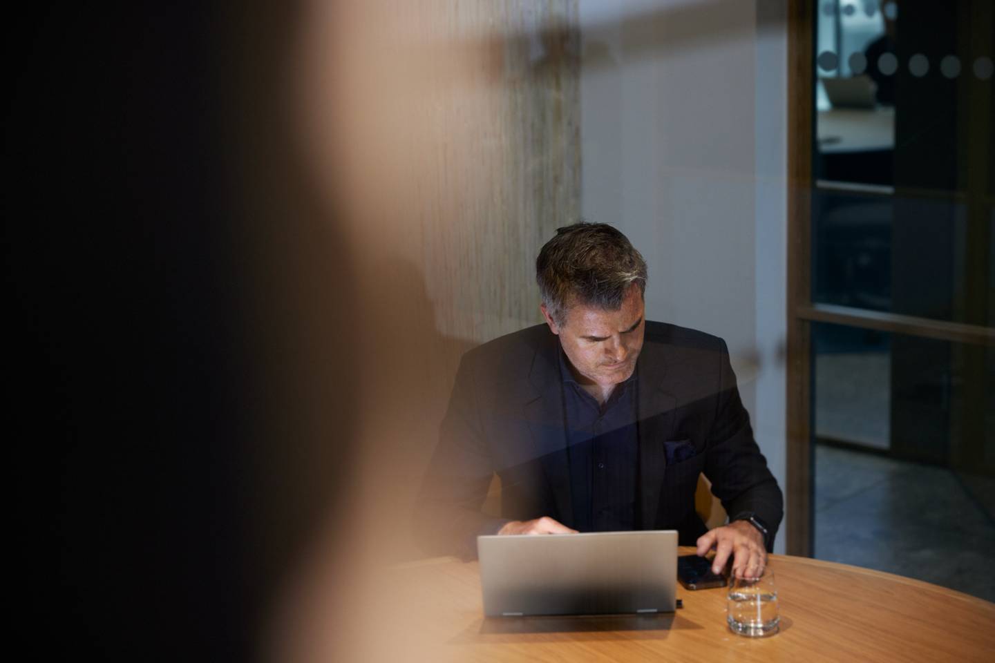 En man sitter vid ett runt bord med en laptop i kontorsmiljö.