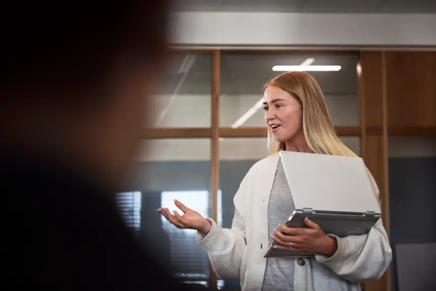 Kvinna står med laptop i famnen i kontorsmiljö.