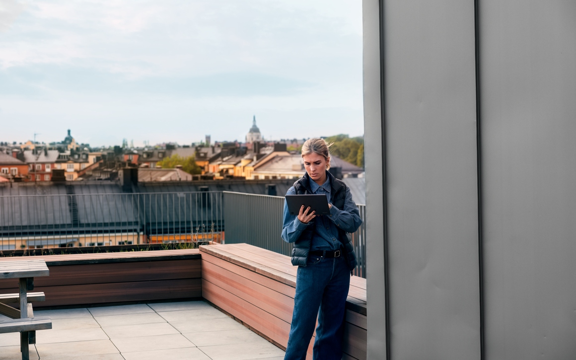 Kvinna med surfplatta på balkong och takåsar i bakgrunden i Stockholm.