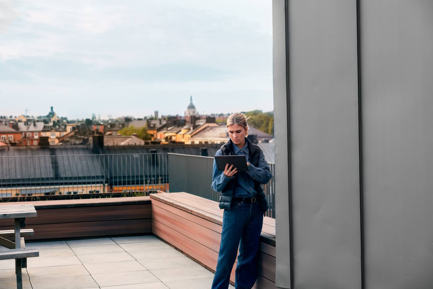 Kvinna med surfplatta på balkong och takåsar i bakgrunden i Stockholm.