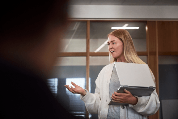 Kvinna står med laptop i famnen i kontorsmiljö.